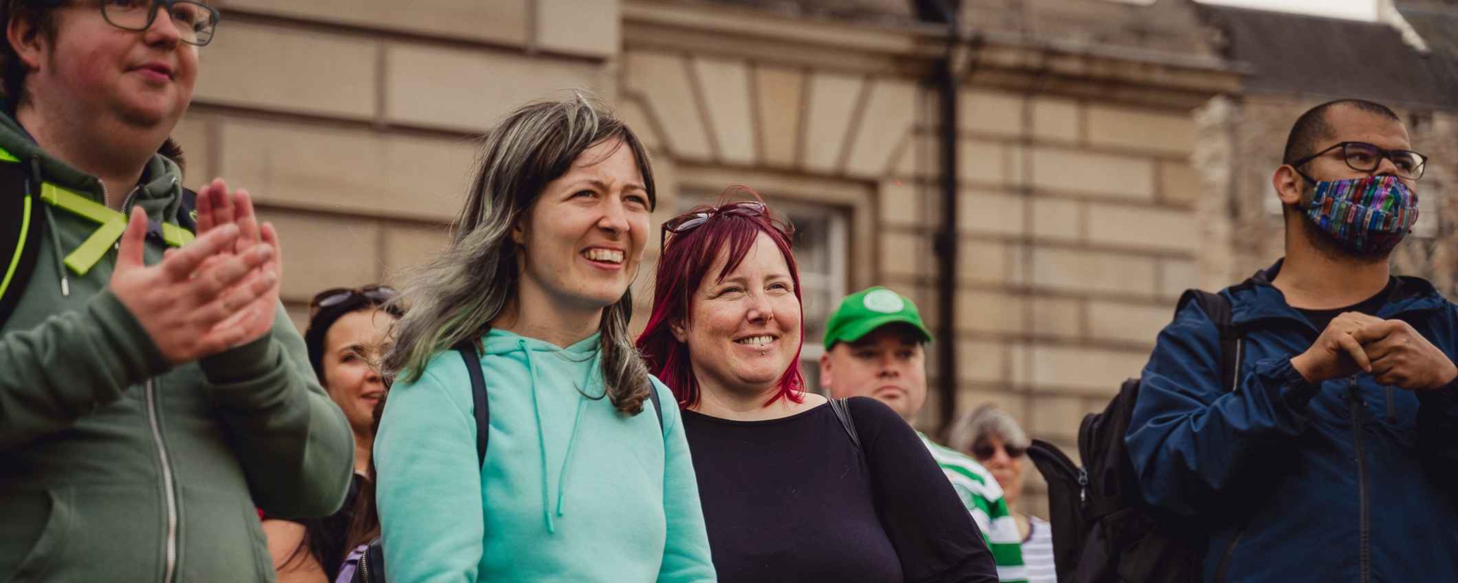 Thera Trust staff and service users standing side-by-side watching an outdoor event, smiling and clapping