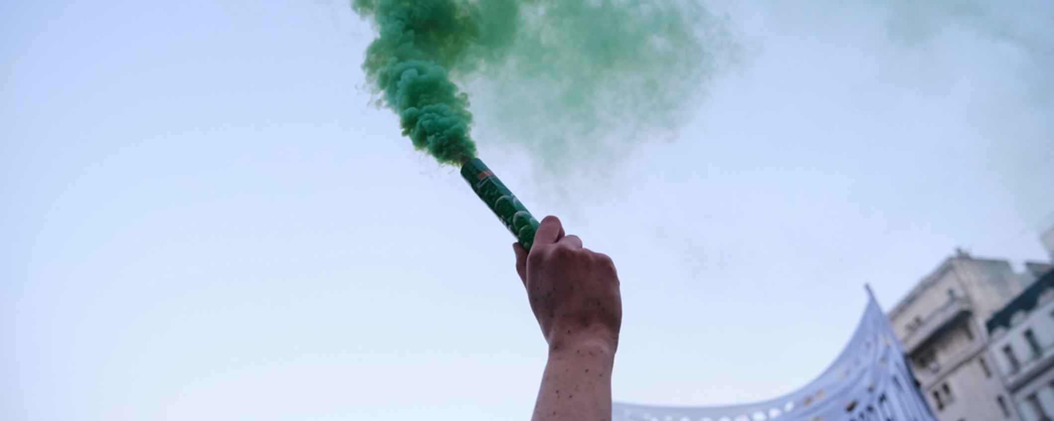 arm raising a green smoke flare at a protest