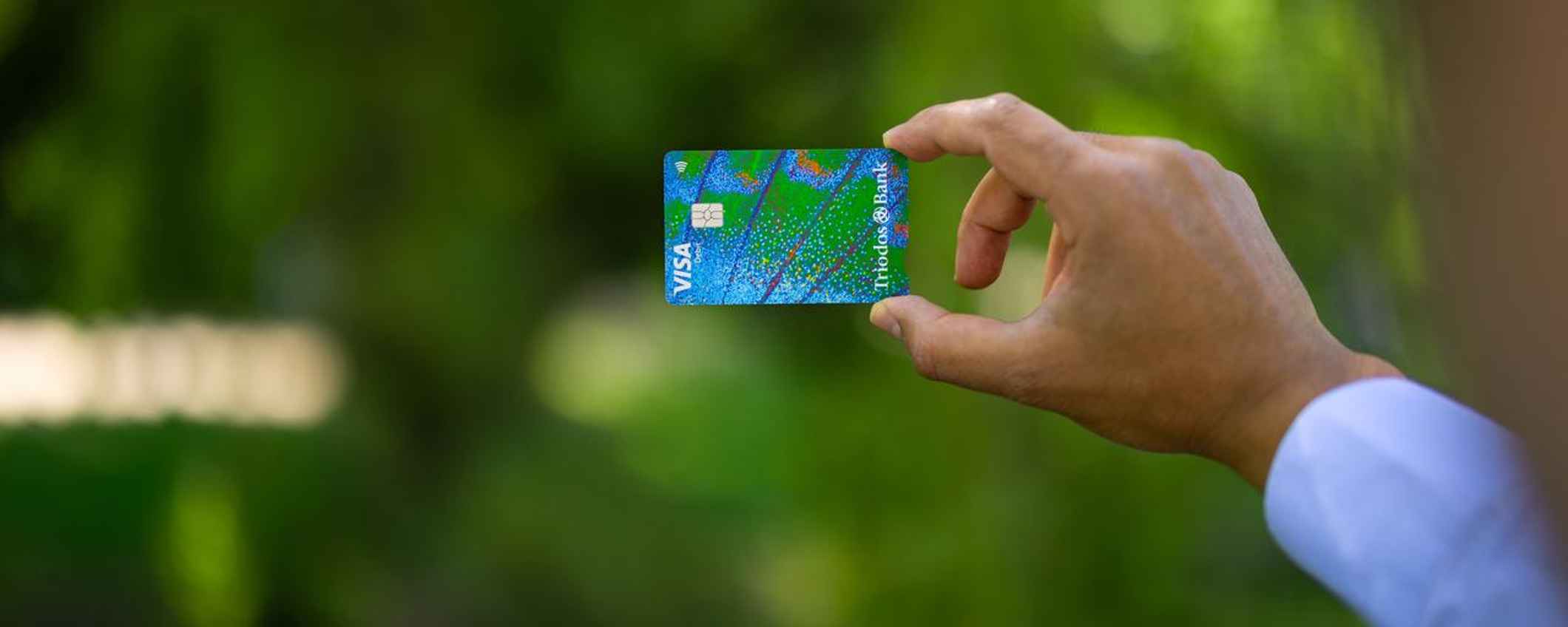 Hand outstretched showing Triodos debit card with metallic blue and green butterfly wing pattern