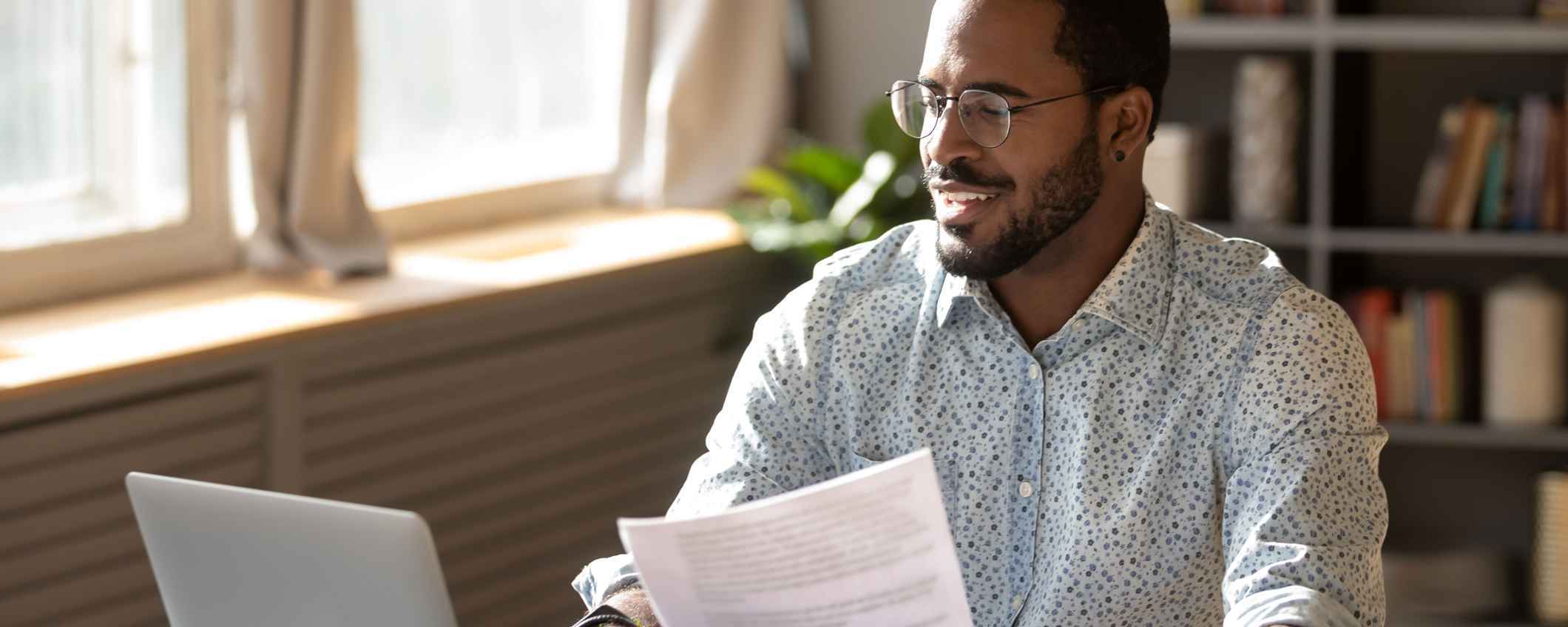Happy man in home office on laptop and looking at paperwork