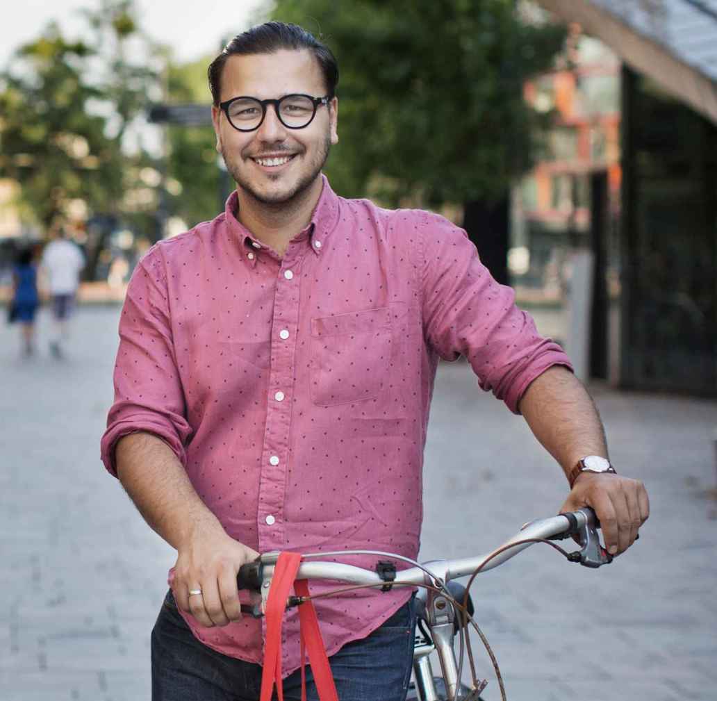 Bearded man with bike in pink shirt and jeans smiling at camera
