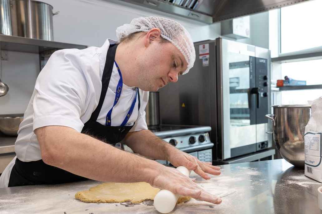 Service user carefully rolling pastry in an industrial kitchen