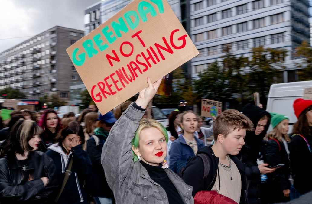 Young activists at a protest, woman holding banner which says greenday not greenwashing